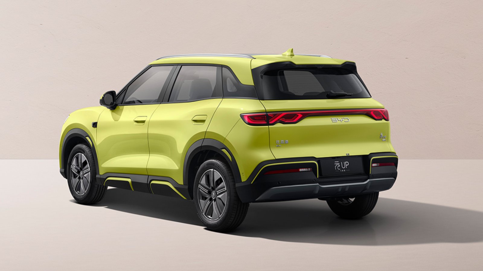 Rear three-quarter view of the yellow 2027 BYD Yuan Up, showing its full-width taillight strip, roof spoiler and black b