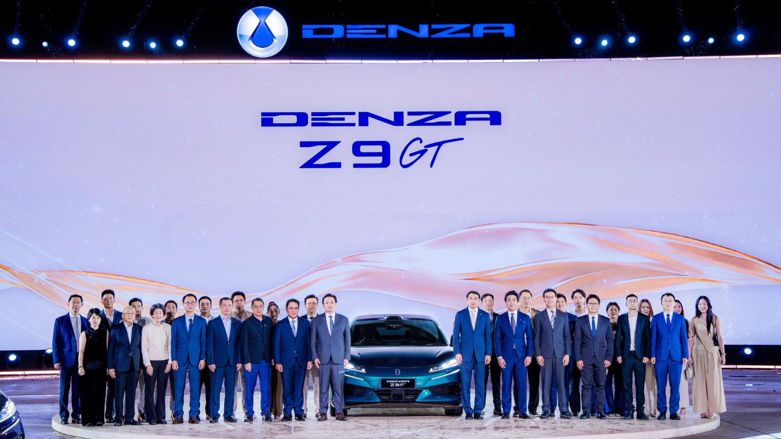 Guests pose around a green Denza Z9GT on stage beneath a large Denza logo at the model’s Thailand launch.