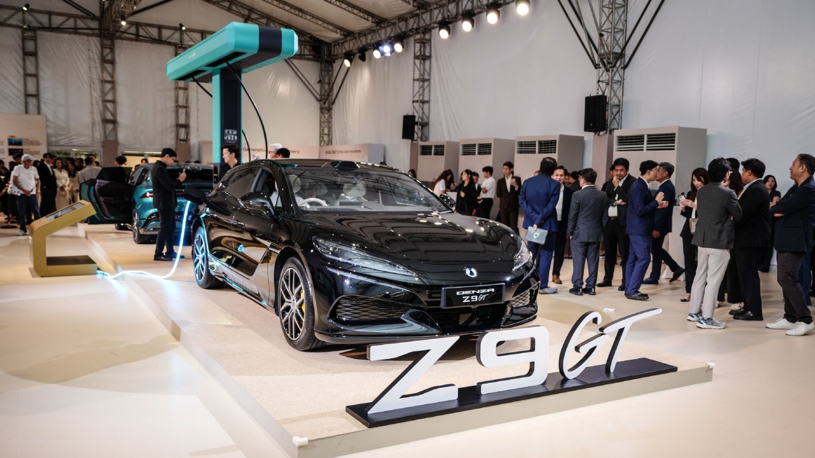 A black Denza Z9GT connected to a flash charger, with attendees gathered around the display at its Thailand launch.