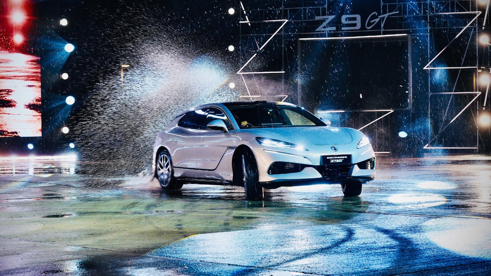 A silver Denza Z9GT drifts across a wet surface, sending up water spray under spotlights at its Thailand launch.