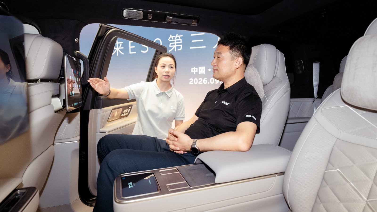 Insnex chairman He Yinjun sits in a Nio ES9's second-row seat as a staff member demonstrates the rear passenger scr